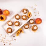 Top view - White tray filled with Peach Almond Muffins with sliced peaches to the side.