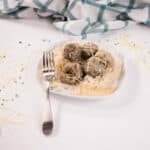 White plate with keto noodles topped with meatballs and parmesan cheese. A white and green hand towel is in the background.