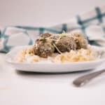White plate with keto noodles topped with meatballs and parmesan cheese. A white and green hand towel is in the background.