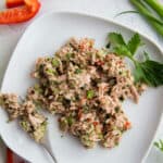 Top view-Tuna salad on a white plate with some on a fork. Plate is surrounded by celery stalks, green onions, and red pepper slices.