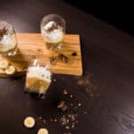 Three glasses of Banoffee Parfaits sitting on a cutting board, one glasslaying on its side