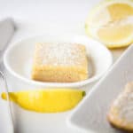 Close up - single square of Lemon Bar on a small white plate. Lemon wedges on the side.
