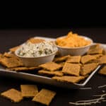 Side view - Chicken Crackers on a white plate with two small bowls of dip.