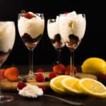Side view - Three glass goblets filled with berries and Lemon Mousse. Surrounded by berries and lemons.
