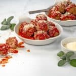 Two white bowls filled with Parmesan Meatballs, topped with marinara sauce. A bowl of parmesan cheese to the side.