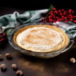 Pie plate with Eggnog Cream Pie. Surrounded by pecans, cranberry boughs, and a green striped dish towel.
