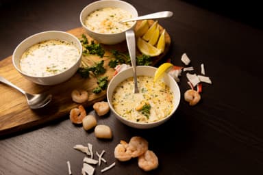 Three white bowls filled with Seafood Bisque. Lemon wedges and shrimp on the side.