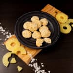 Black plate filled with Coconut Macaroons. Sliced pineapple on the side.