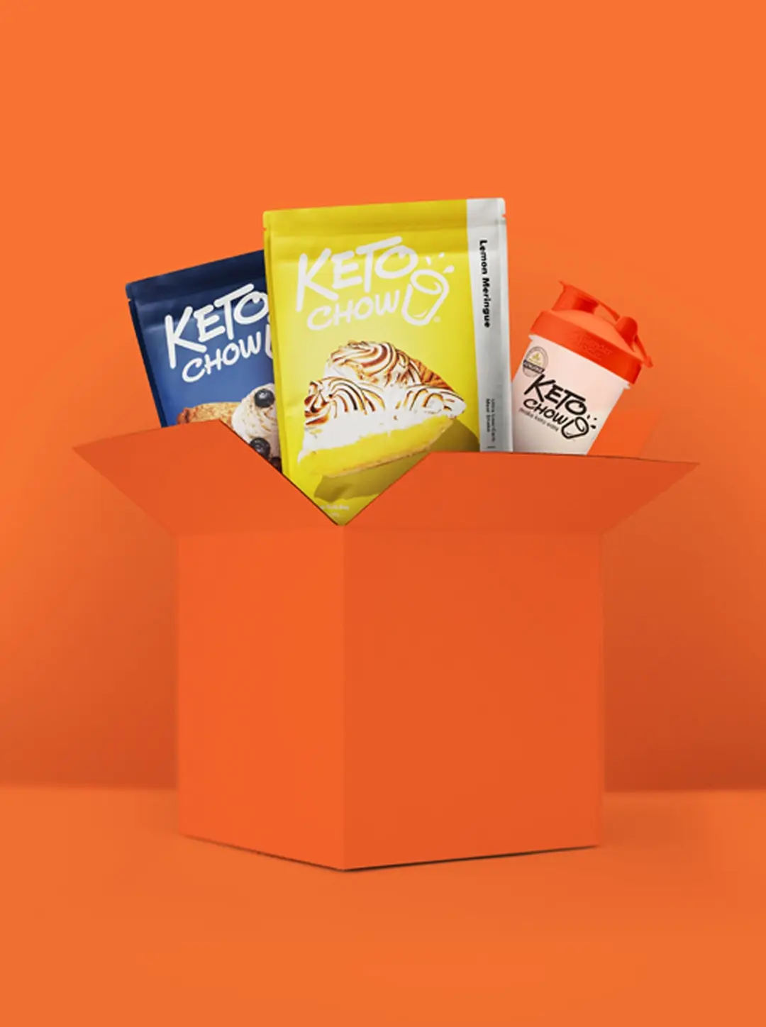 Keto Chow subscription bundle with two colorful meal mix bags—one in bright yellow labeled Lemon Meringue and a second navy blue bag with an unreadable flavor—alongside a white Keto Chow shaker bottle with an orange lid, all emerging from an orange box against a bold orange background.