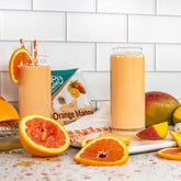 two Orange Mango shakes with oranges and mangos around them